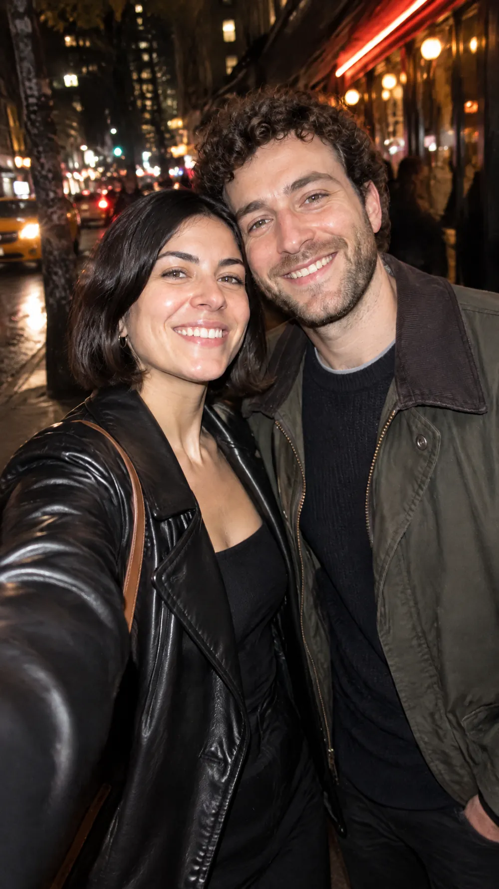 Night flash photo of a couple in jackets smiling on a city street, lit by a bright on-camera flash with dark surroundings