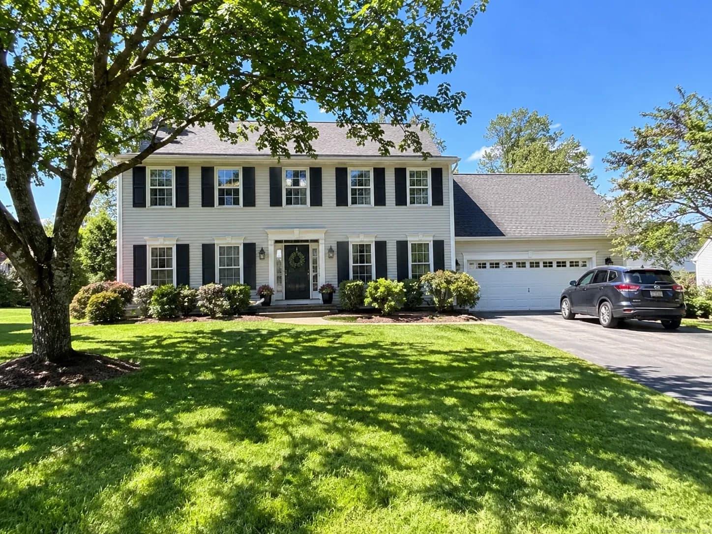 Original daytime photo of the same house with a green lawn and blue sky